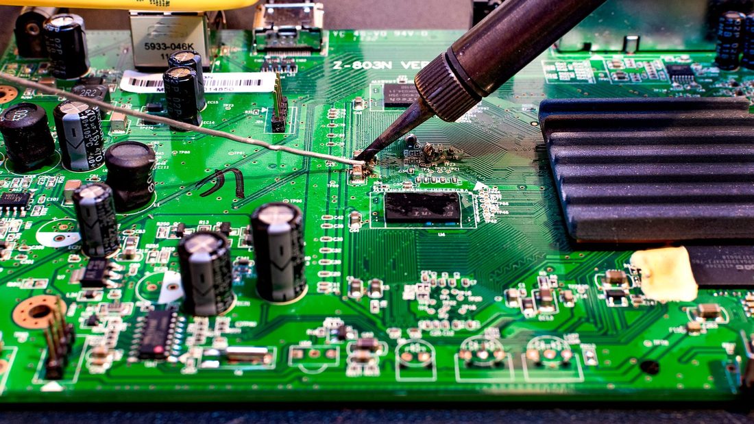 Nomadic TV Repairs technician soldering a television circuit board during a component-level repair